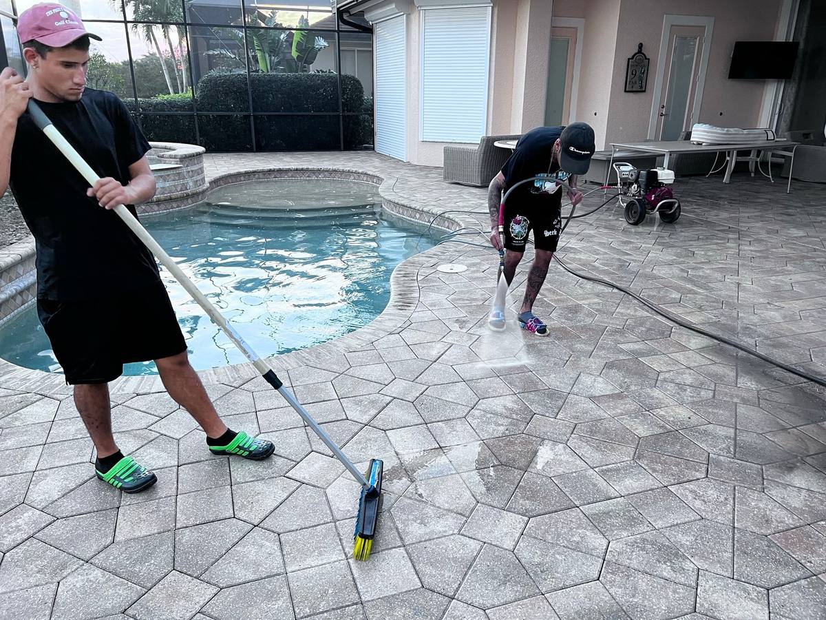 Paver Savers crew sweeping joint sand and pressure cleaning a paver pool deck