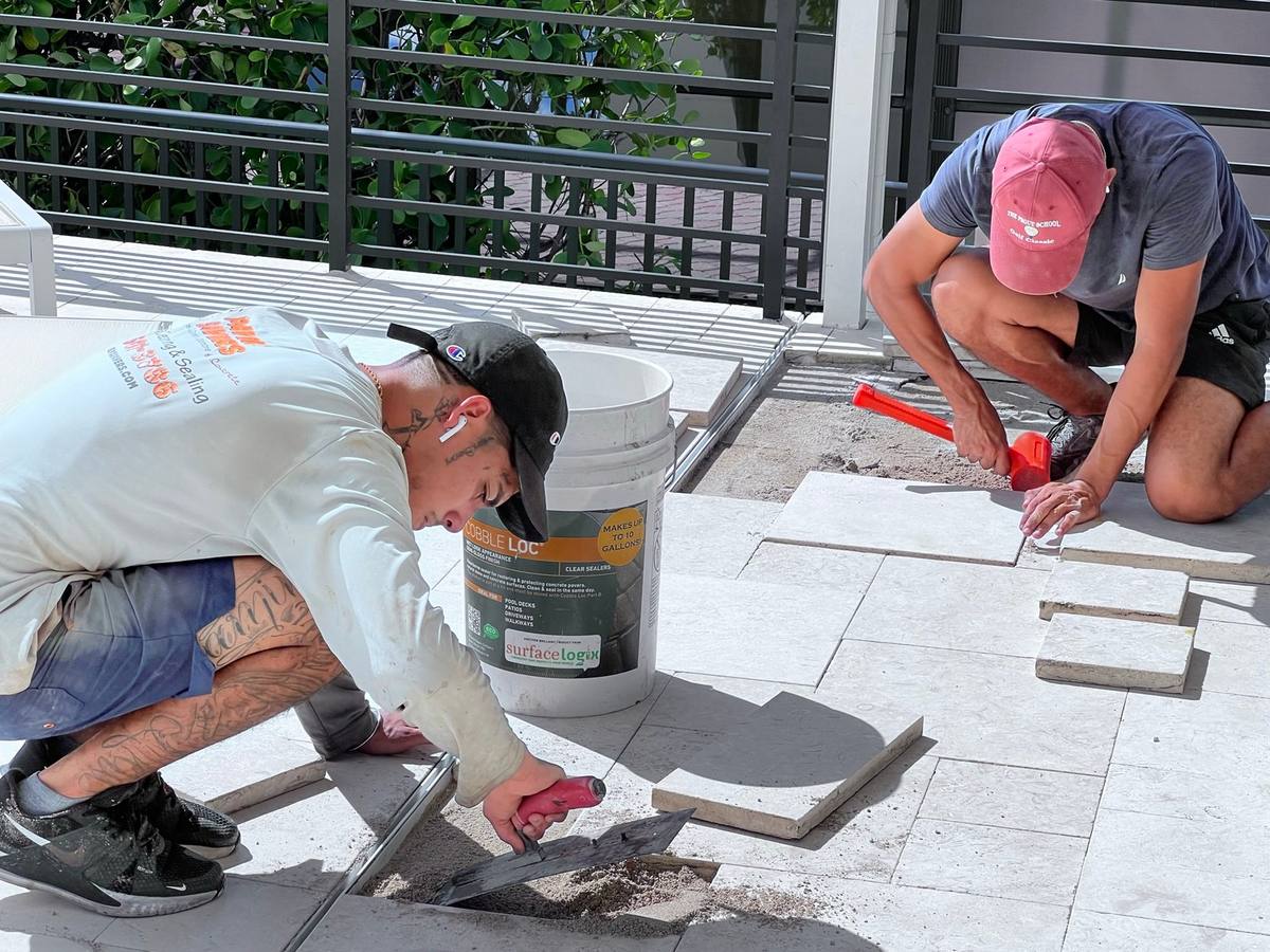 Two Paver Savers crew members cutting and setting travertine pavers on a pool deck