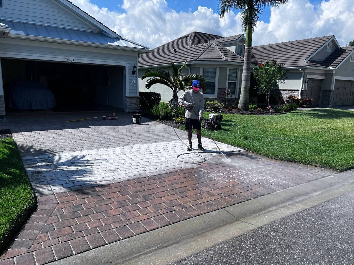 Driveway mid-strip: the far pavers still chalky white with failed sealer, the near pavers stripped back to rich red
