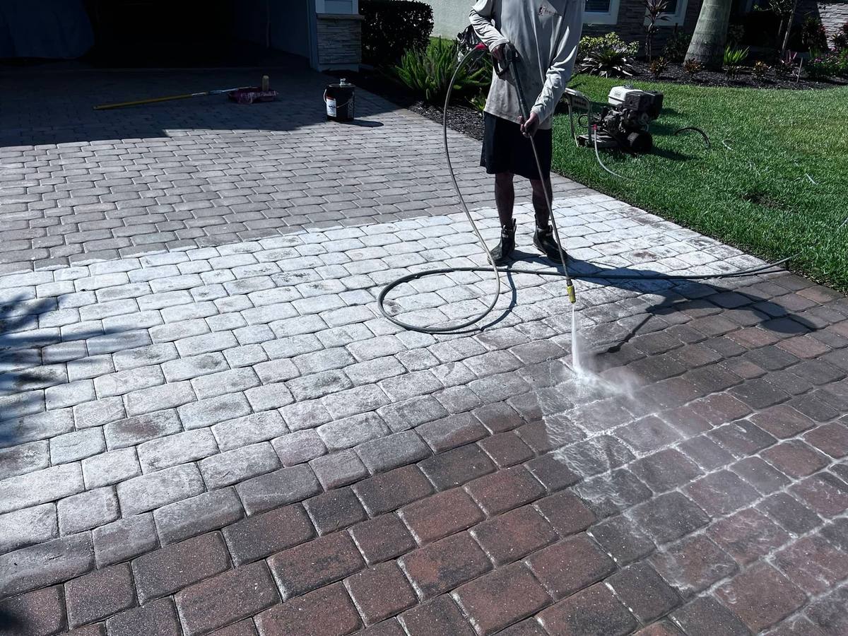 Crew member stripping old sealer from a paver driveway, with the cleaned half clearly brighter than the untouched half