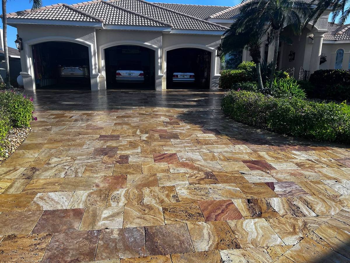 Cleaned and sealed golden travertine driveway in front of a three-car garage